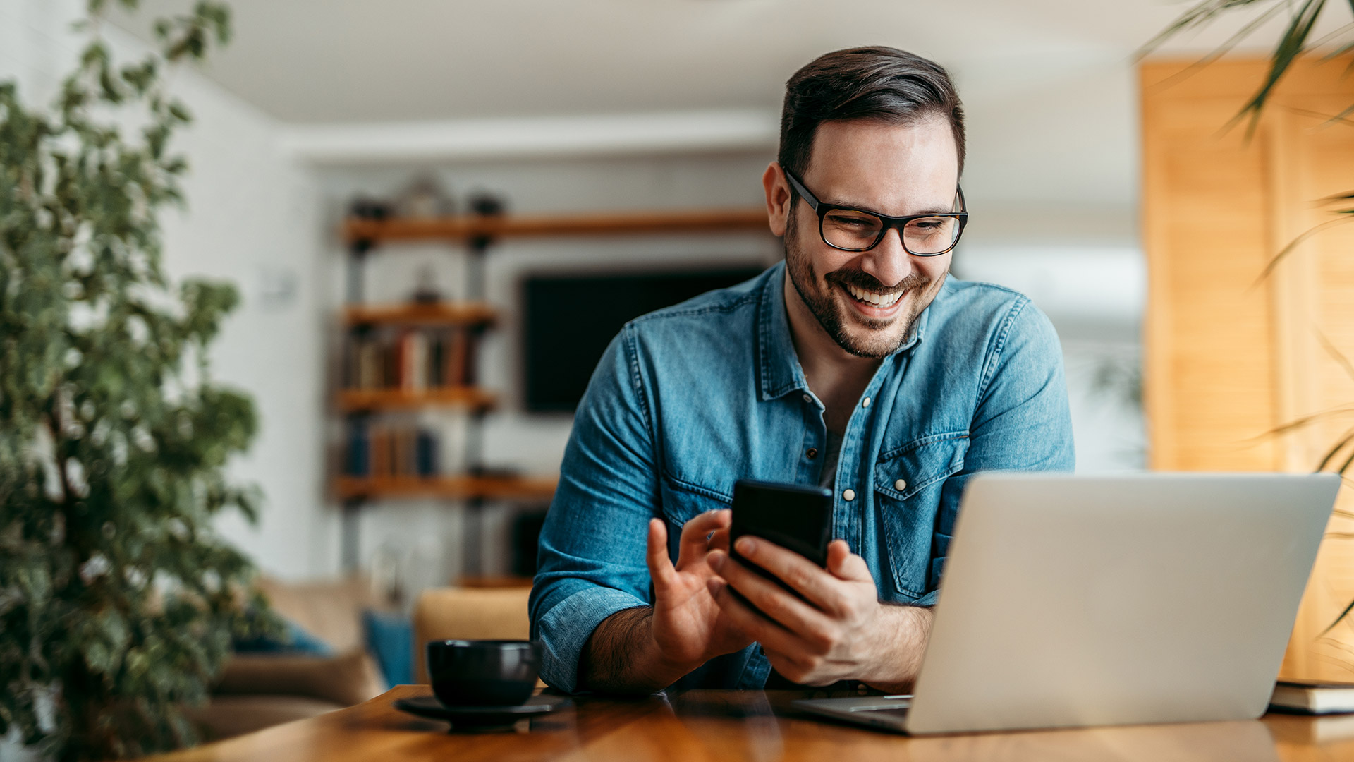 Happy man at home using phone and laptop